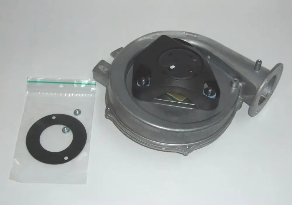 Daikin Ventilator-Einheit aus Metall, montiert auf einer Basis mit einem schwarzen Kunststoff-Aufsatz und Schrauben, daneben eine Dichtung und Befestigungselemente in einer Kunststofftüte.